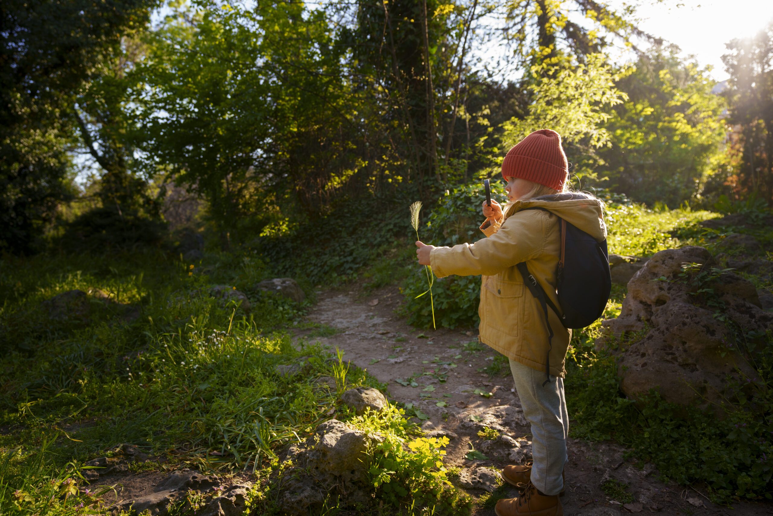 Enfant explorant la nature avec une fleur à la main, dans un sentier boisé.