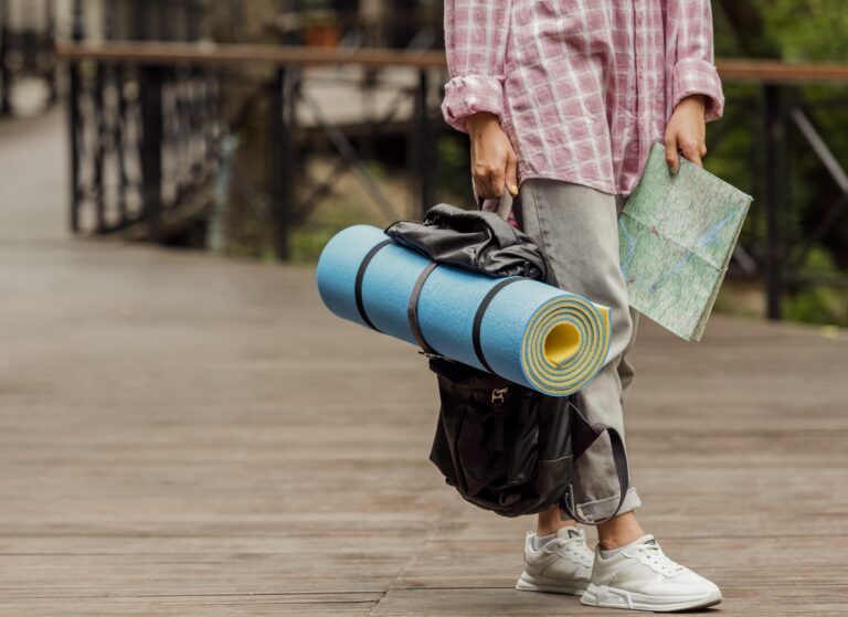 Personne tenant un tapis de randonnée bleu et une carte, prête pour une excursion en plein air.