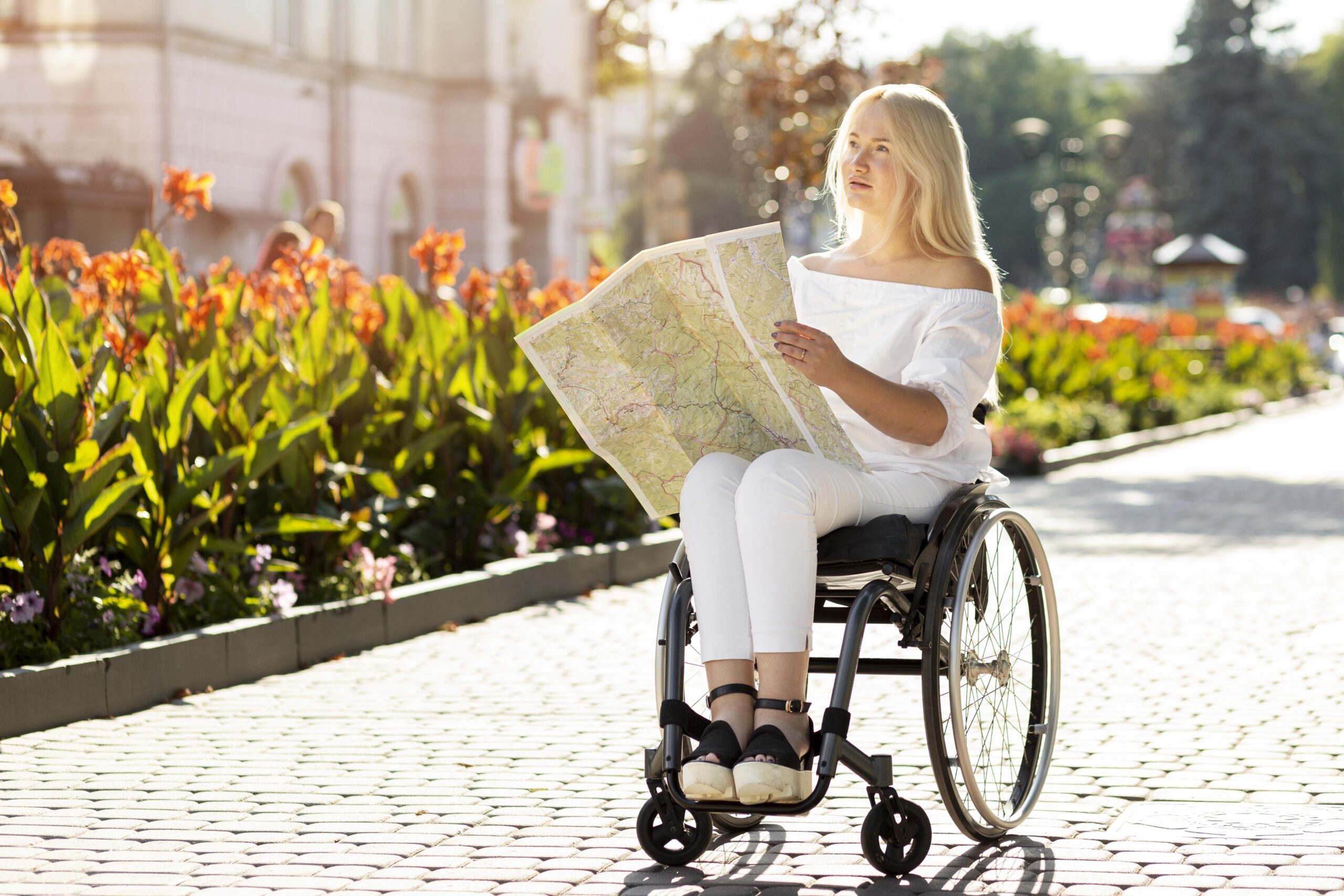 Femme en fauteuil roulant lisant une carte dans un espace urbain fleuri par une journée ensoleillée