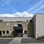 Façade moderne du gîte Le Clos Nestor à Xhoffraix, combinant pierre et bois, avec une entrée accessible aux personnes à mobilité réduite.